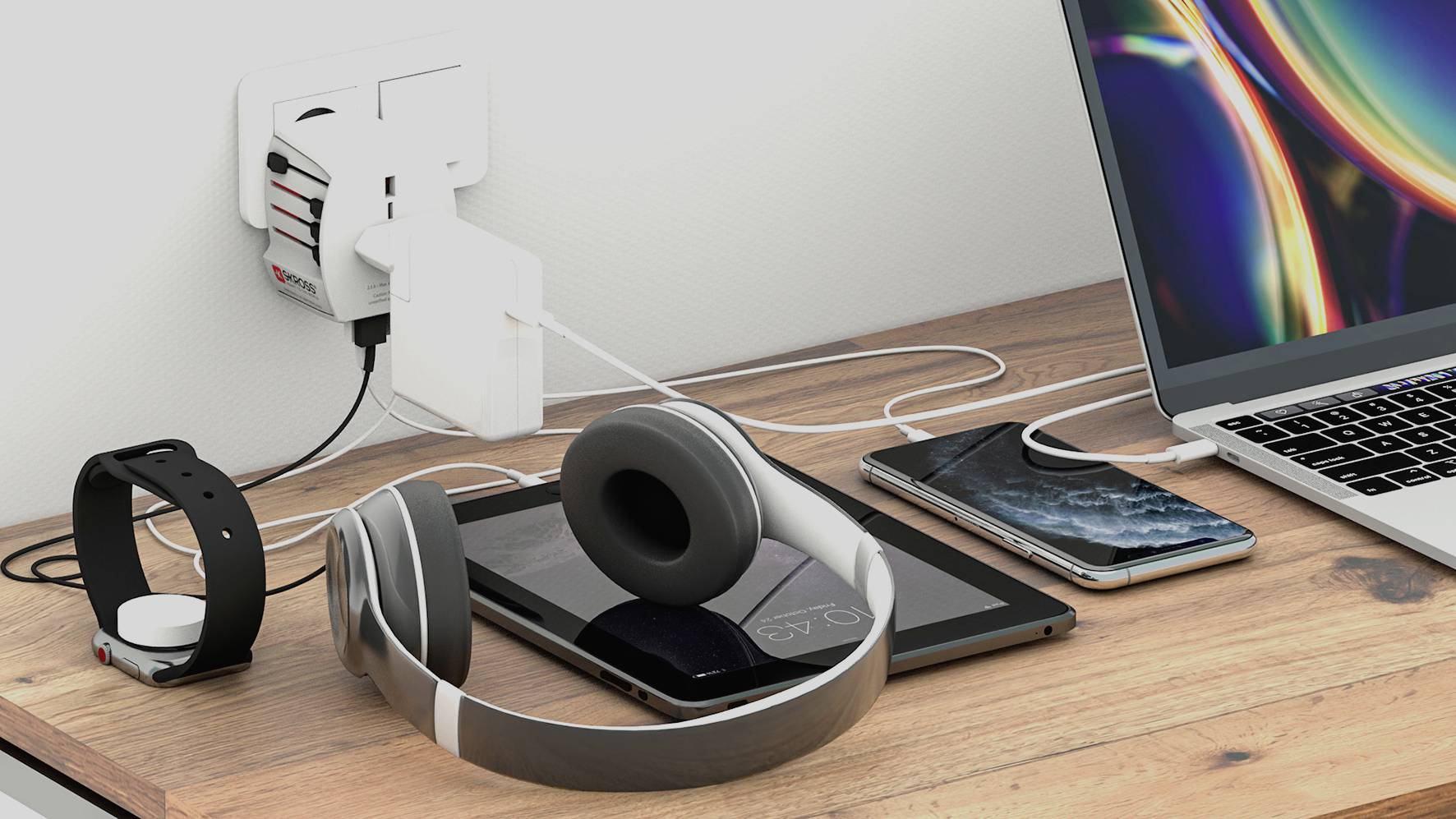 Stůl s různými elektronickými zařízeními: laptop, smartphone, tablet, sluchátka a nabíječky připojené k elektrické zásuvce.