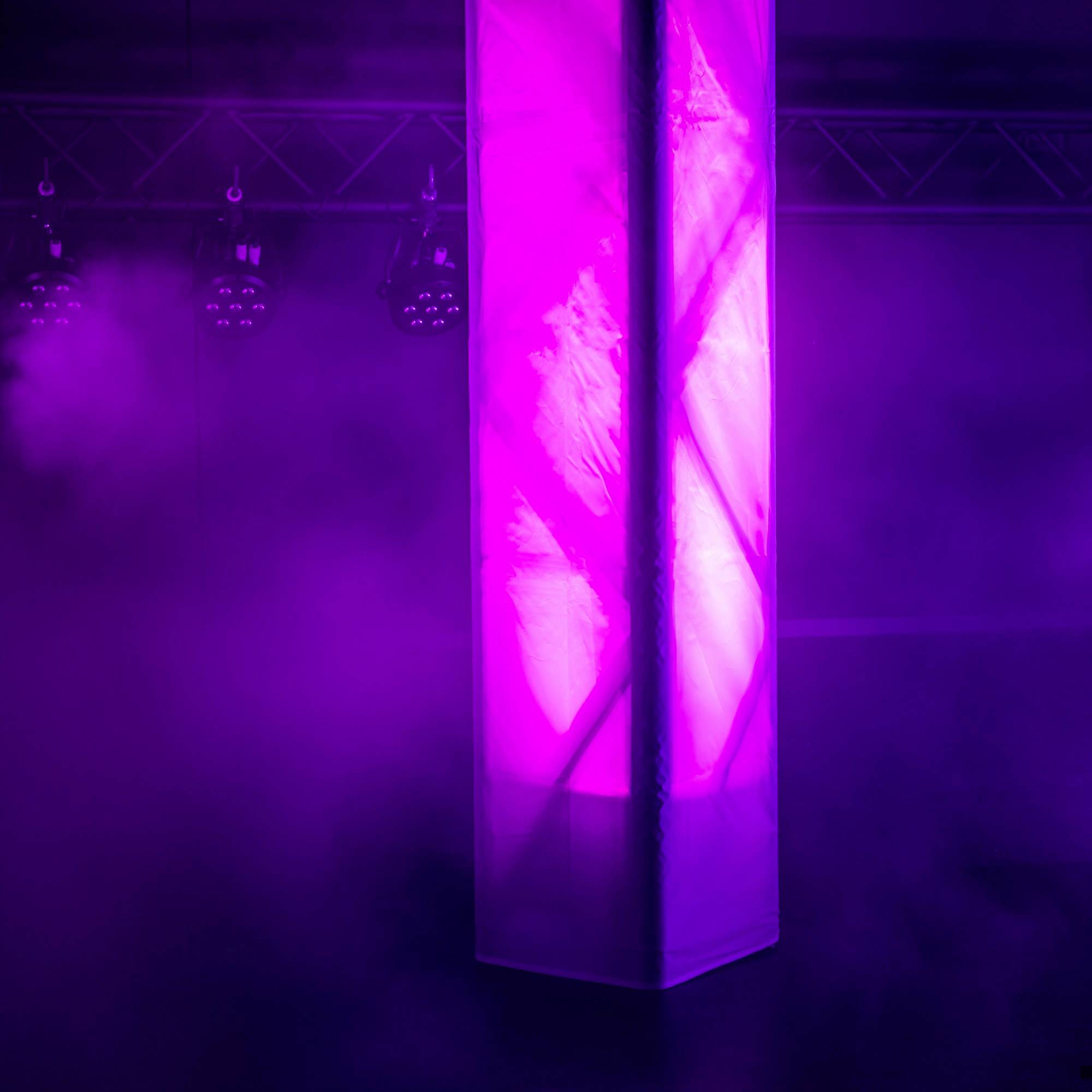 Vysoký, zářící sloup v místnosti s fialovým světlem a mlhou, obklopený reflektory vytvářejícími mystickou atmosféru.