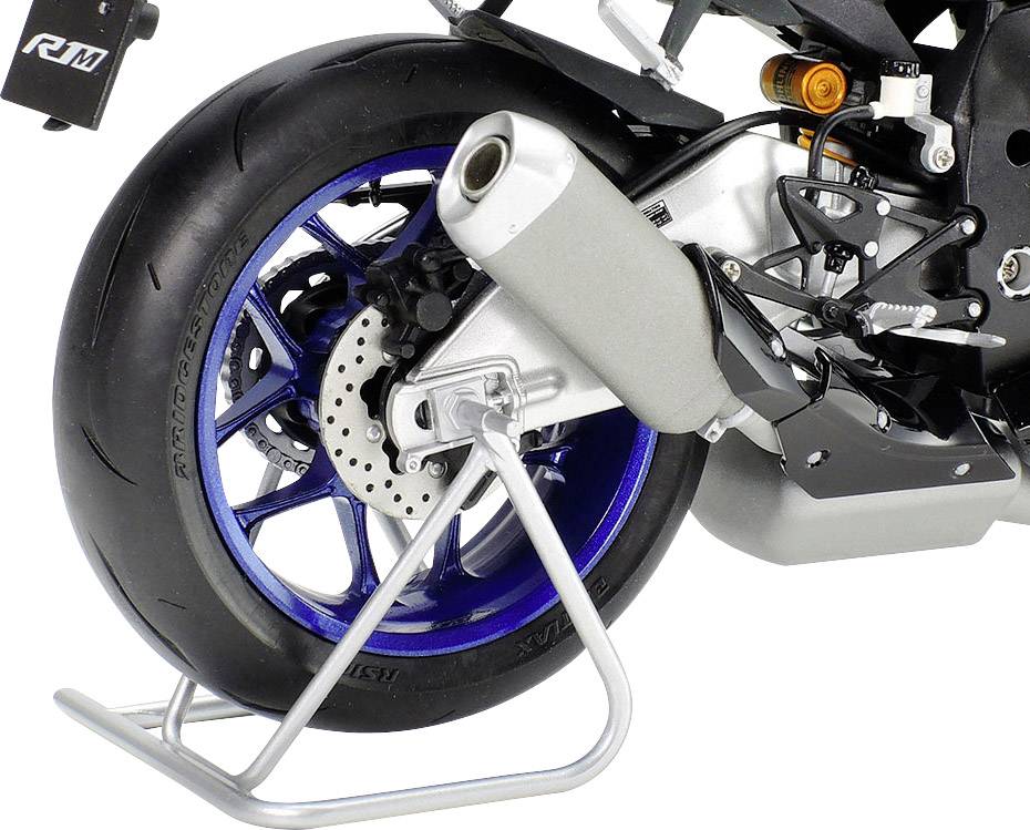 Zadní kolo motocyklu s modrým designem ráfku a výfukem. Motocykl stojí na stříbrném stojanu.