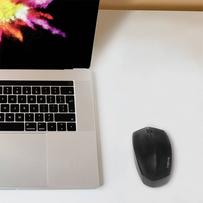 Laptop s barevnou explozí na obrazovce vedle černé bezdrátové myši na bílém stole.