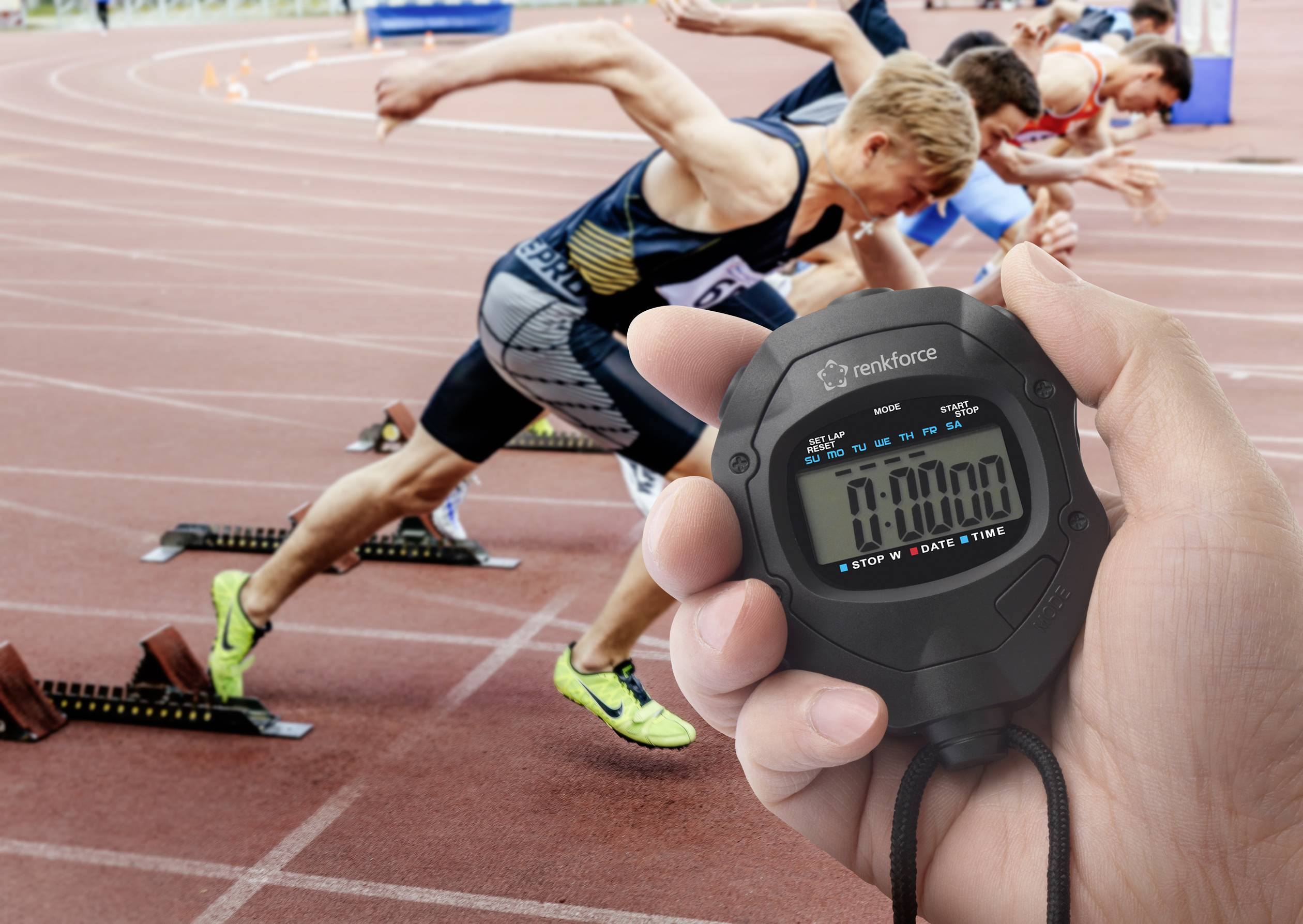 Běžci startují na atletické dráze, zatímco ruka v popředí drží stopky ukazující nulu vteřin, což symbolizuje začátek závodu.