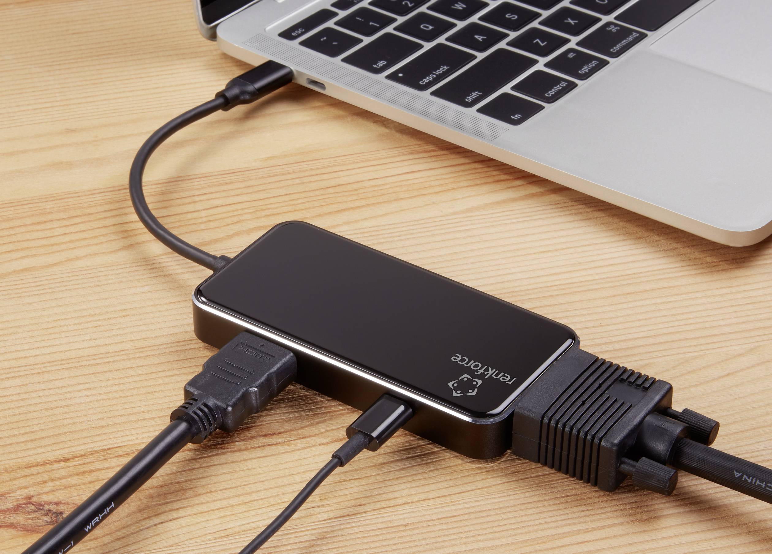 Laptop je připojen pomocí několika kabelů k černému adaptéru, který podporuje HDMI, USB a Ethernet.