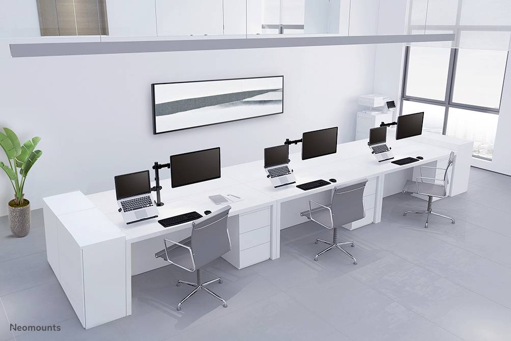 Moderní, minimalistická kancelář se čtyřmi pracovními místy. Každé pracovní místo je vybaveno monitorem, notebookem a kancelářskou židlí. V pozadí se nachází tiskárna.