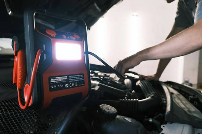 Jedna osoba používá přenosné startovací zařízení k nastartování automobilu s otevřenou kapotou motoru.