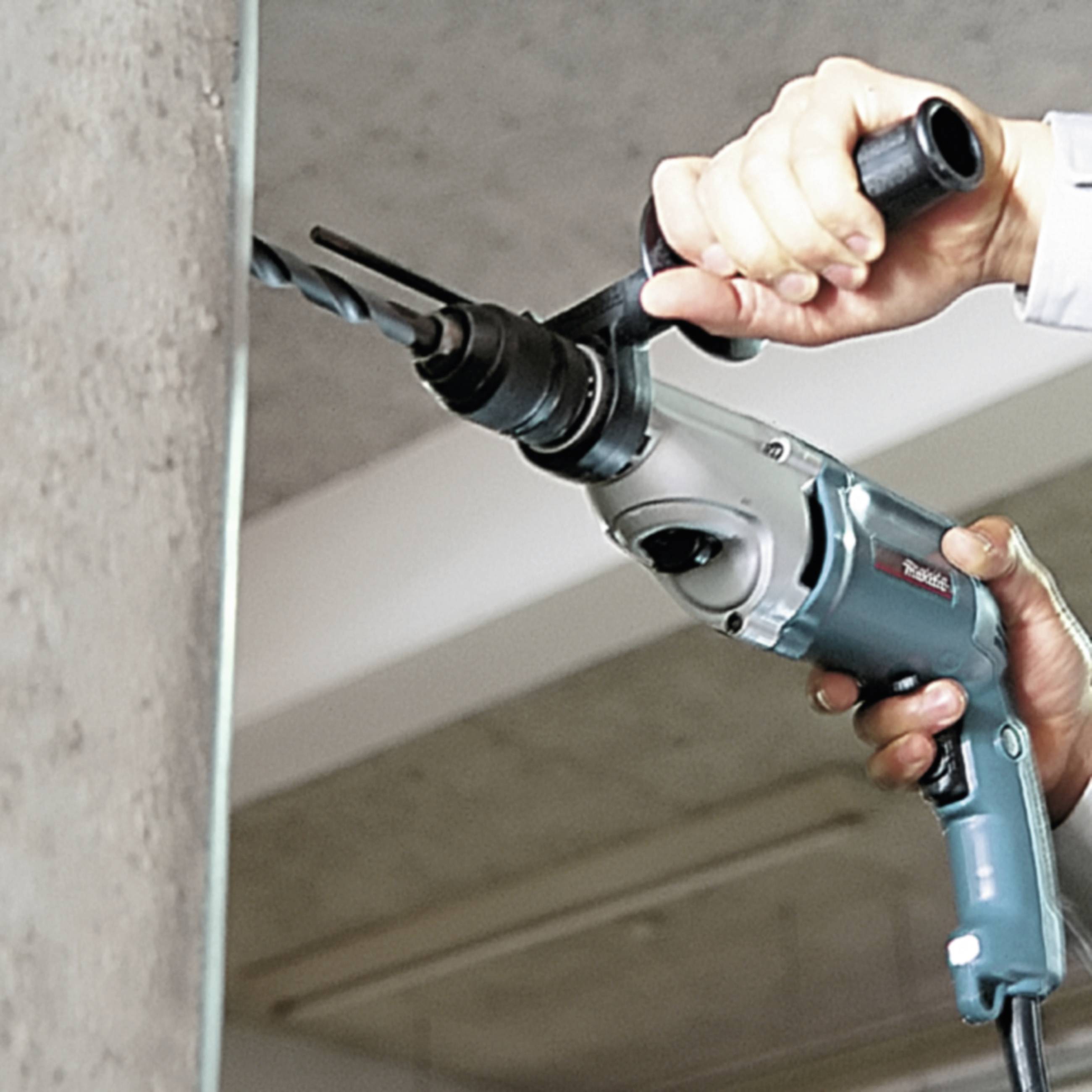 Osoba vrtá elektrickou vrtačkou díru do zdi.