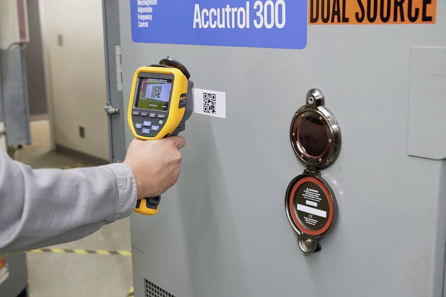 Osoba používá přenosné zařízení ke skenování QR kódu na velkém označeném elektrickém rozvaděči.