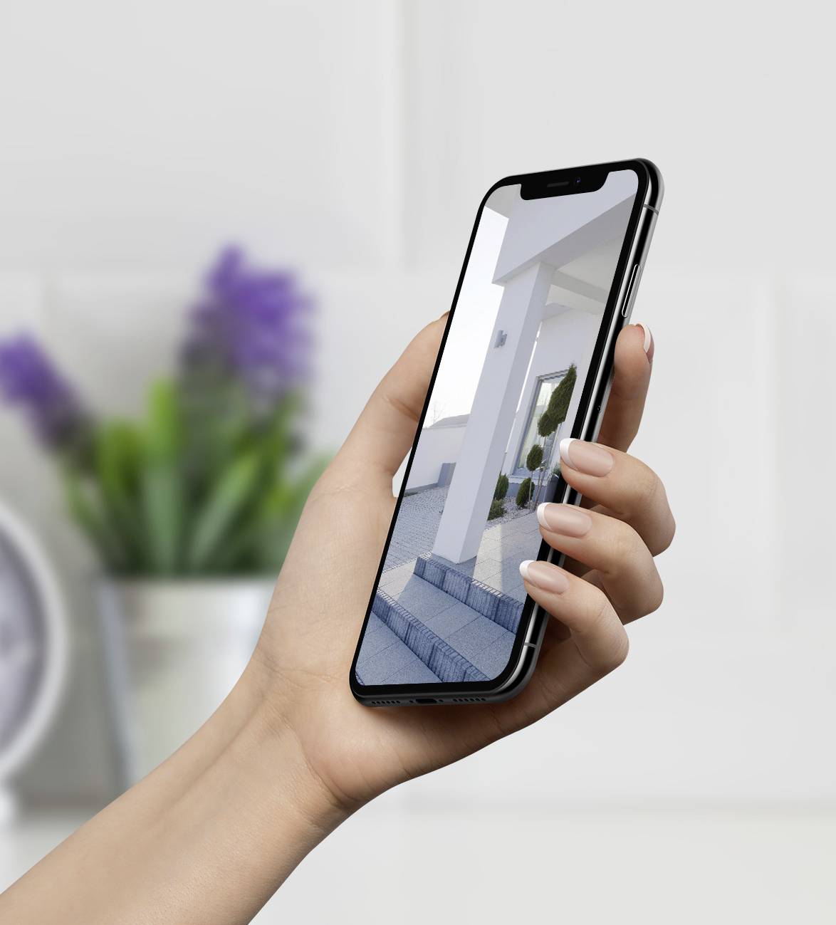 Osoba drží smartphone, na jehož displeji je zobrazen snímek moderní architektury. V pozadí je rozmazaná pokojová výzdoba.