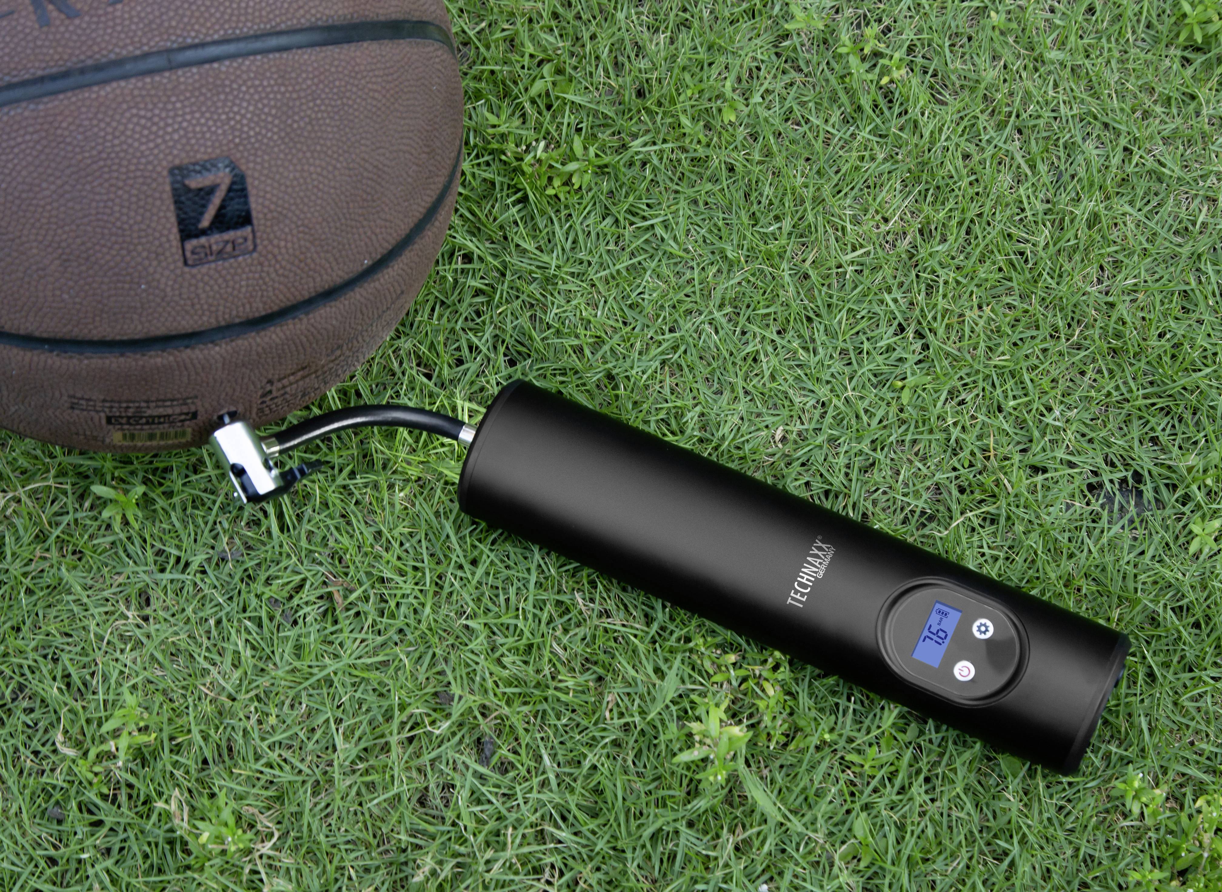 Basketbalový míč leží na trávě vedle černé elektrické vzduchové pumpy s digitálním displejem, který ukazuje tlak 3,5 baru.