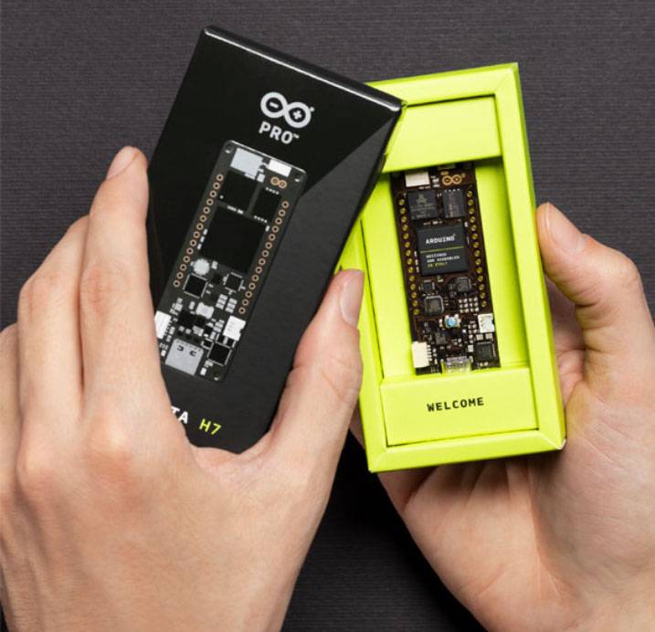 Osoba drží obal a vyjímá desku Arduino, na které je napsáno 'Welcome'.
