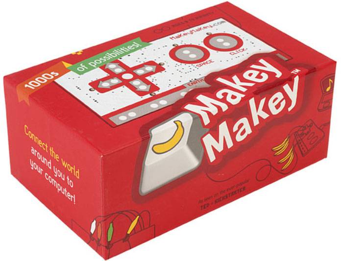 Červená krabice "Makey Makey". Ukazuje elektronickou sadu, která umožňuje kreativní propojení běžných předmětů s počítačem.