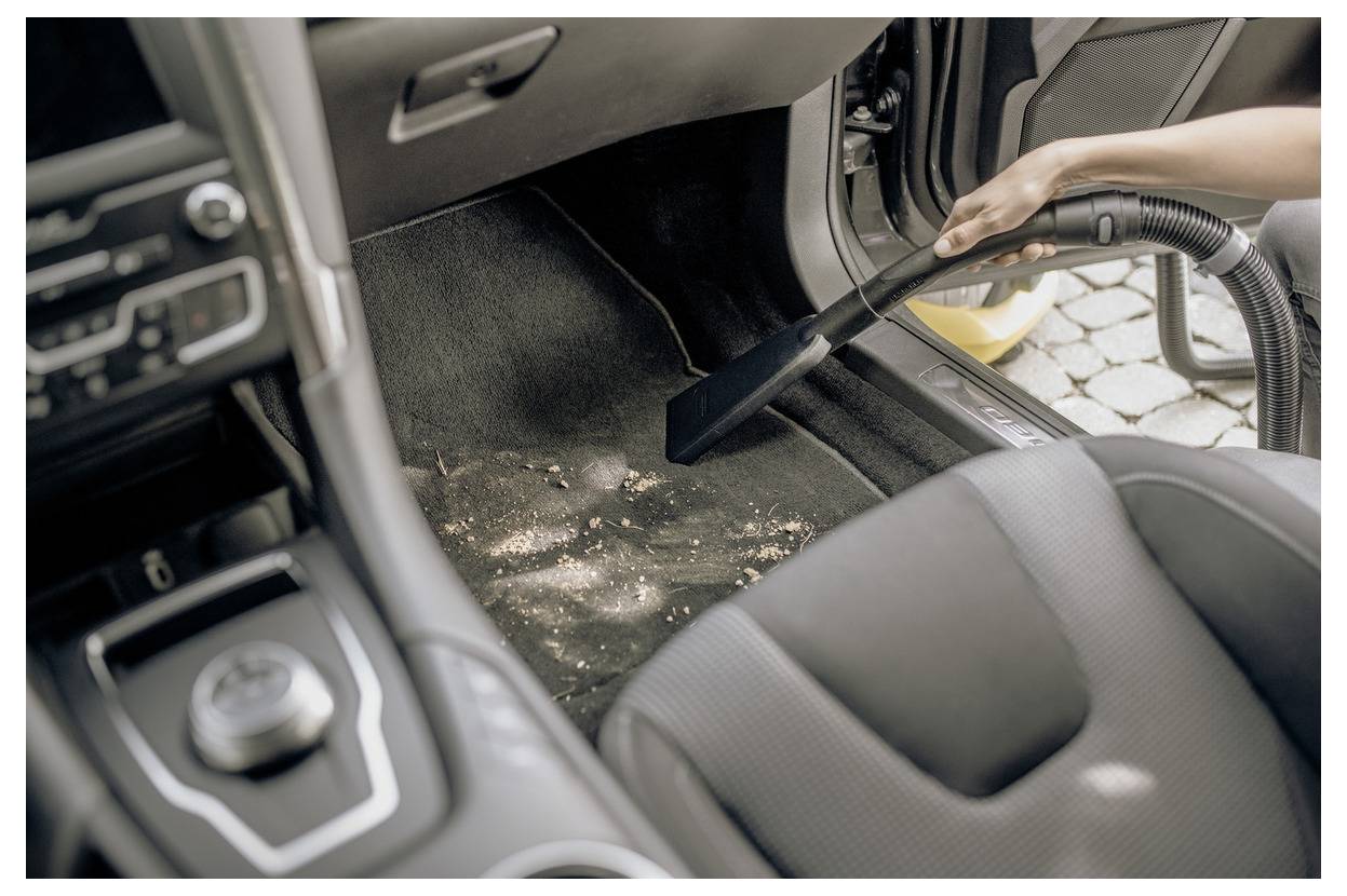 Osoba používající vysavač na podlaze interiéru automobilu, odstraňující nečistoty z koberce.