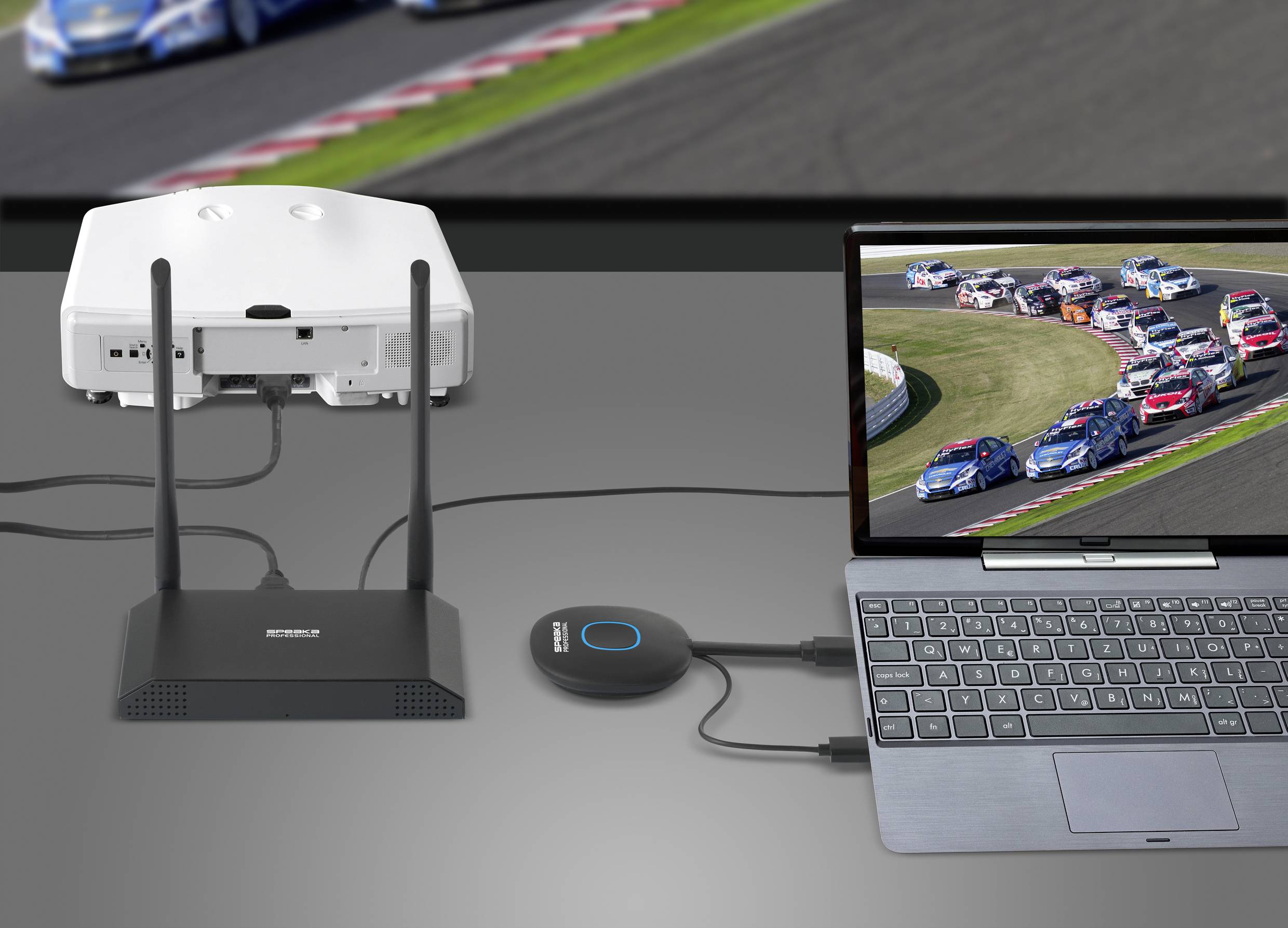 Laptop je bezdrátovým zařízením propojen s projektorem, který zobrazuje automobilový závod. Projektor promítá obraz na plátno.