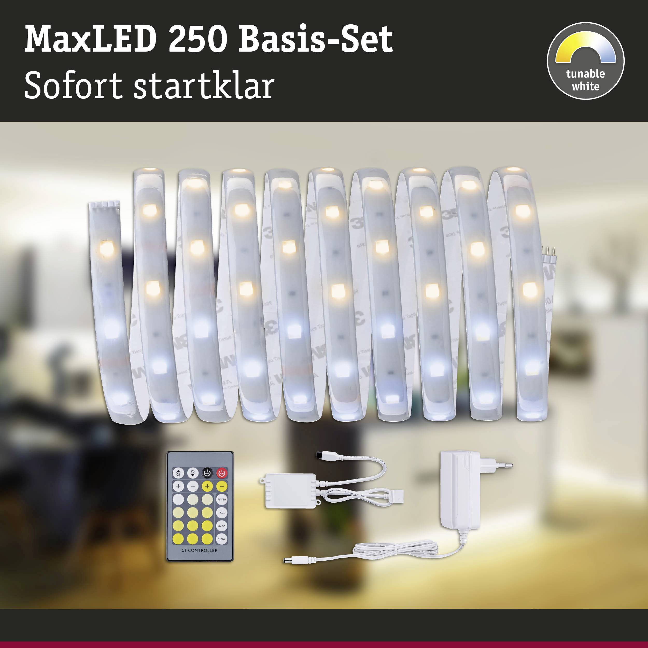 MaxLED 250 základní sada: Bílý LED pásek, dálkový ovladač a napájecí zdroj na obrázku. Pozadí zobrazuje rozmazaný obytný prostor.