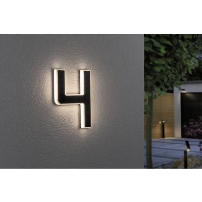 Domovní číslo '4' svítí za soumraku na zdi, obklopeno cestičkou v zahradě a moderní architekturou v pozadí.