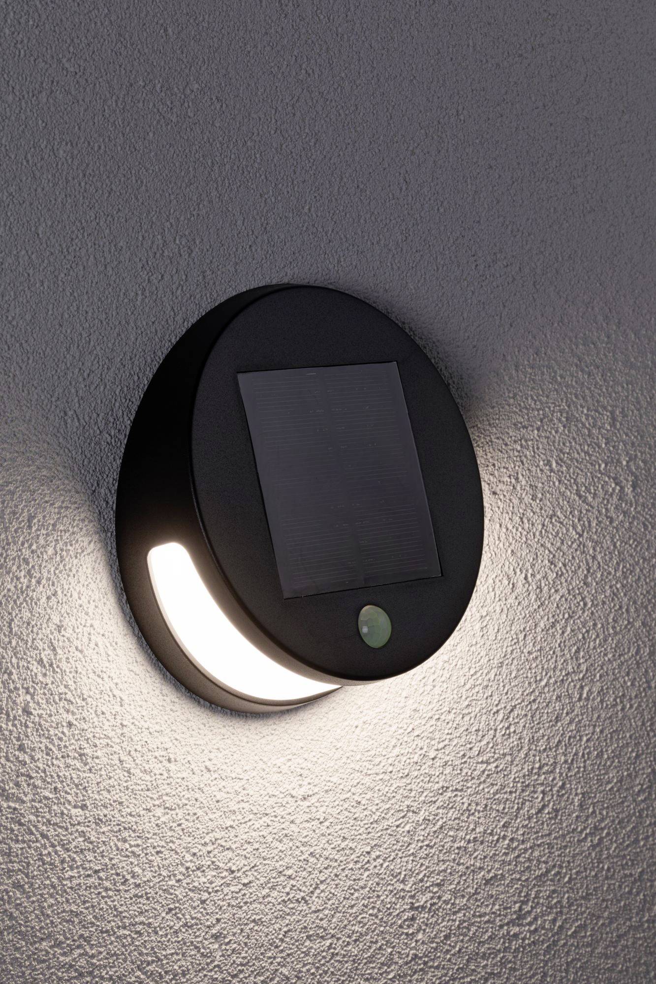 Moderní kulaté venkovní osvětlení s integrovaným solárním panelem, umístěné na zdi. Ideální pro energeticky úsporné osvětlení zahrady.