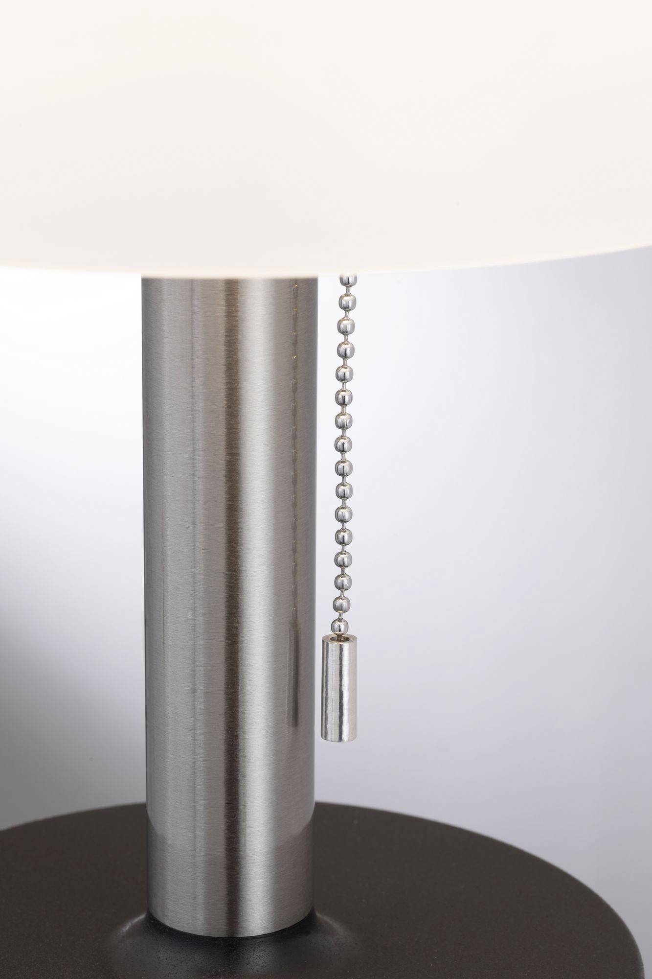 Kovová lampa se šňůrovým spínačem před šedým pozadím.