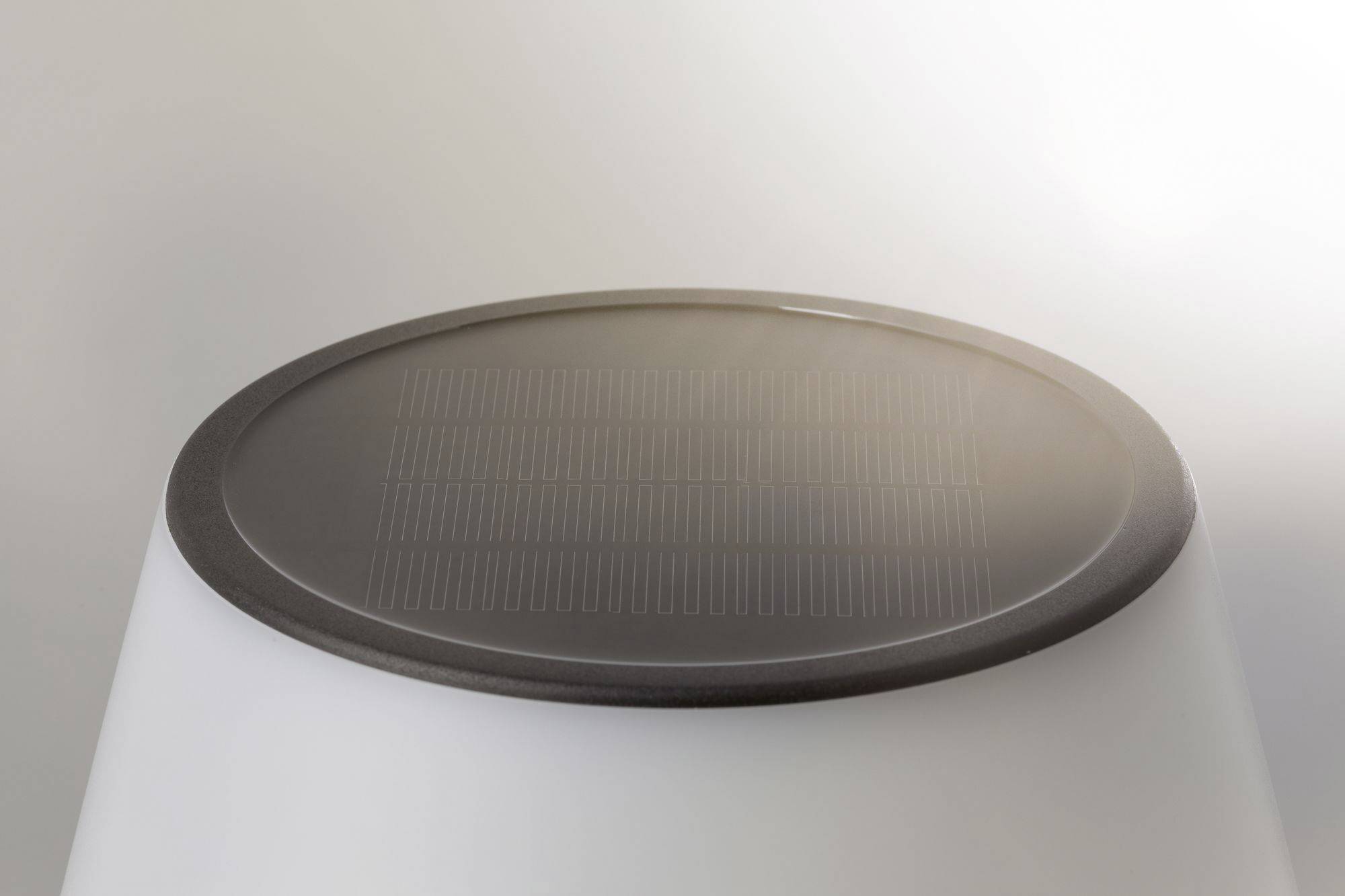 Kulatý solární modul na bílé lampě v minimalistickém designu, osvětlený přirozeným světlem.