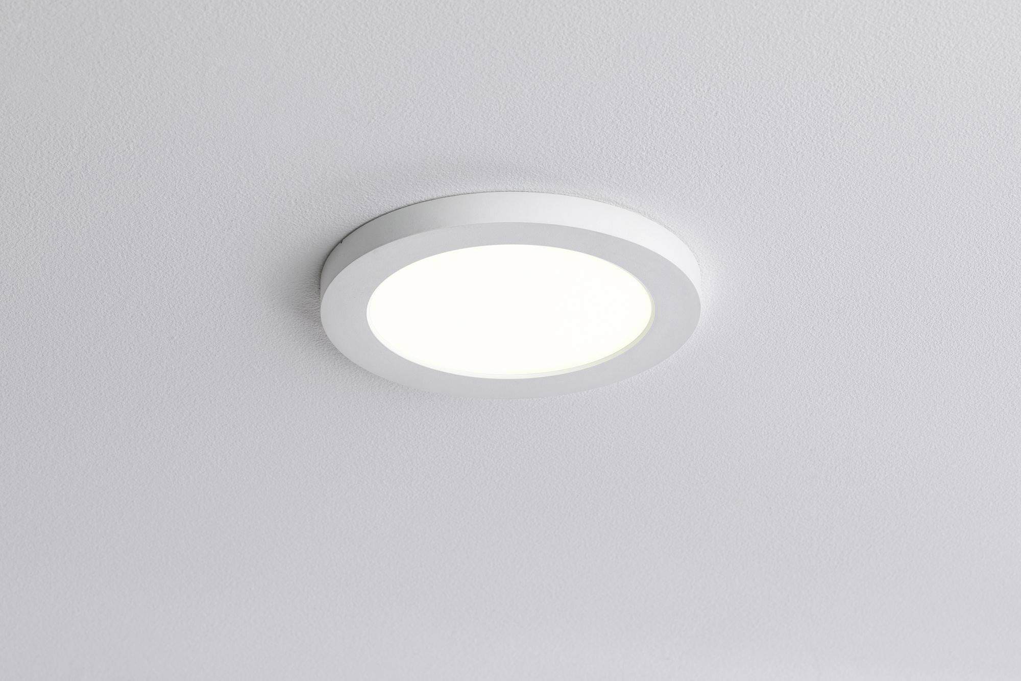 Kulatá stropní lampa s bílým rámečkem jasně svítí na bílém stropě místnosti.