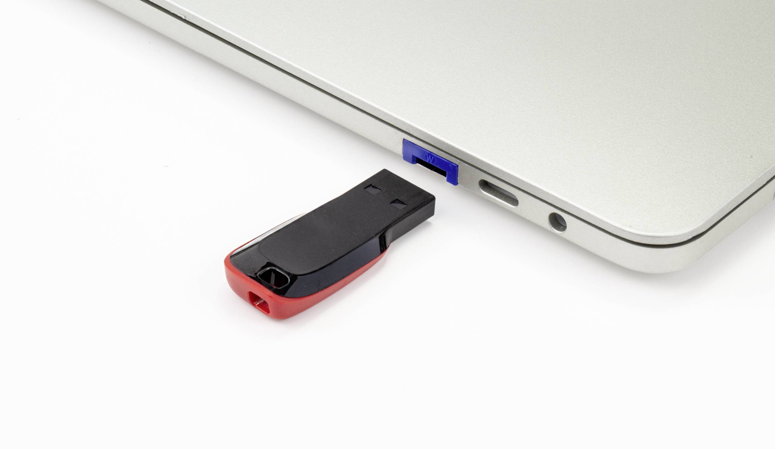 USB flash disk je zasunut do USB portu stříbrného notebooku.