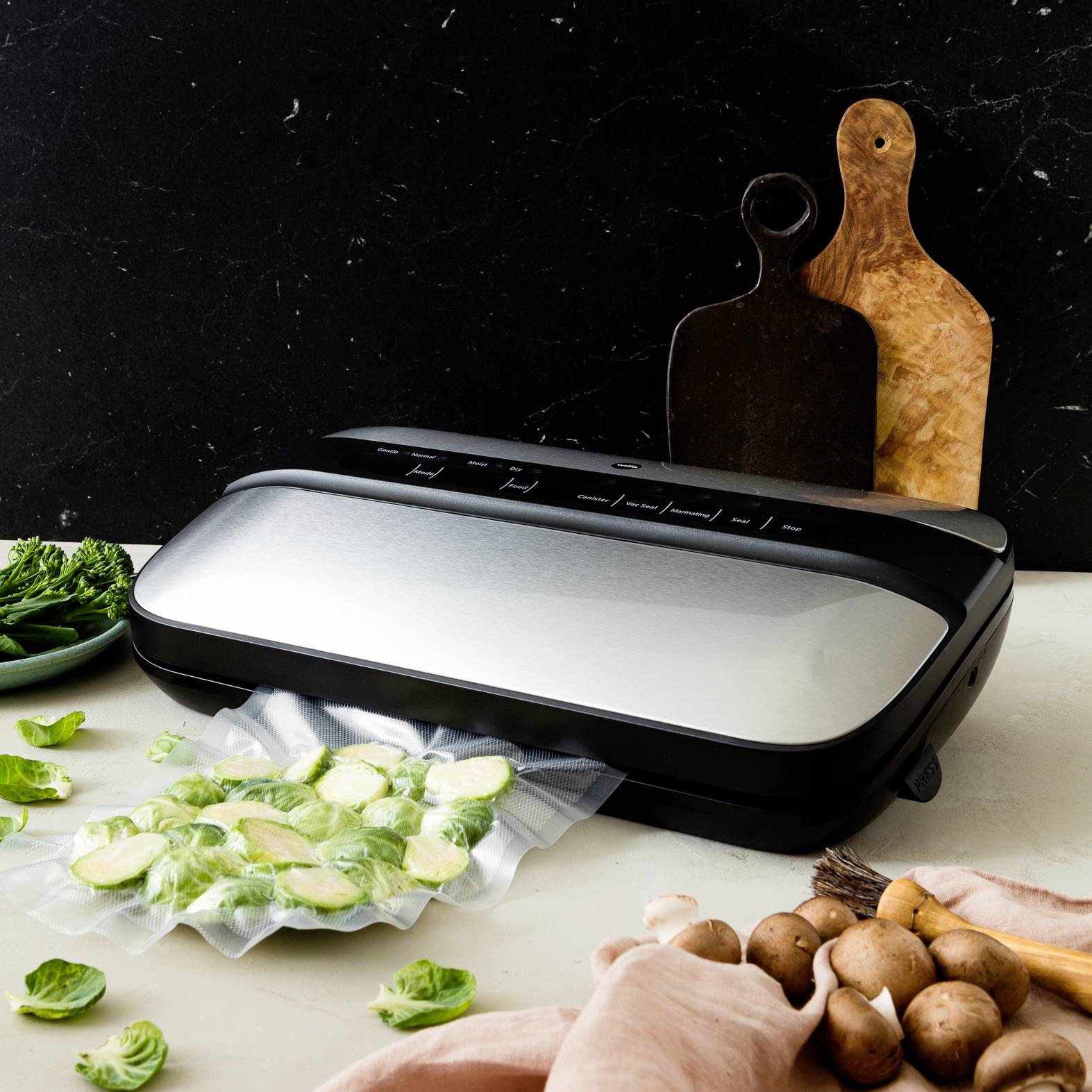 Vakuovací přístroj na kuchyňské pracovní desce při těsnění nakrájené zeleniny, obklopený dalšími čerstvými ingrediencemi.