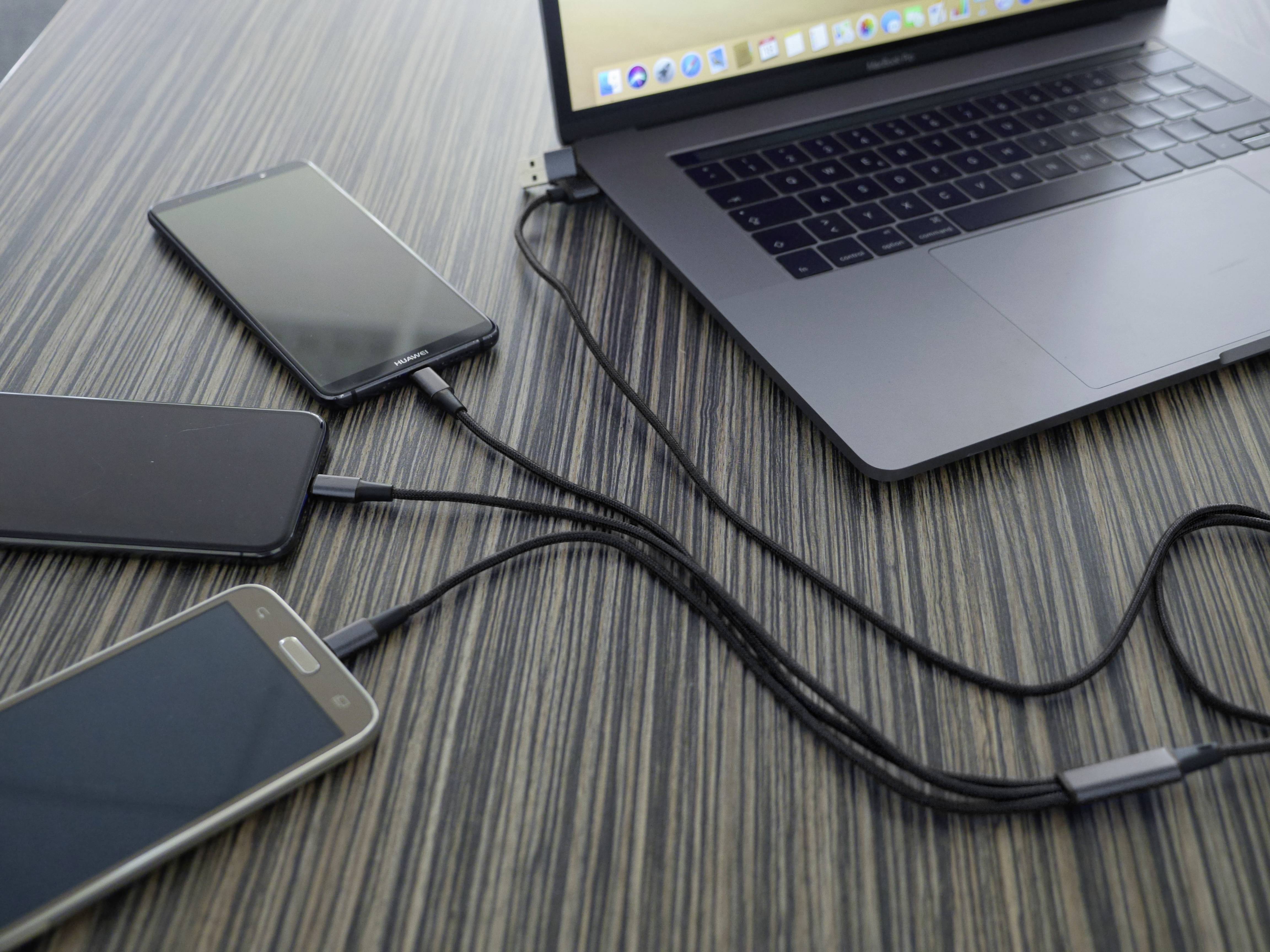 Laptop na stole, připojený ke třem smartphonům pomocí USB kabelů. Všechna zařízení jsou současně nabíjena.