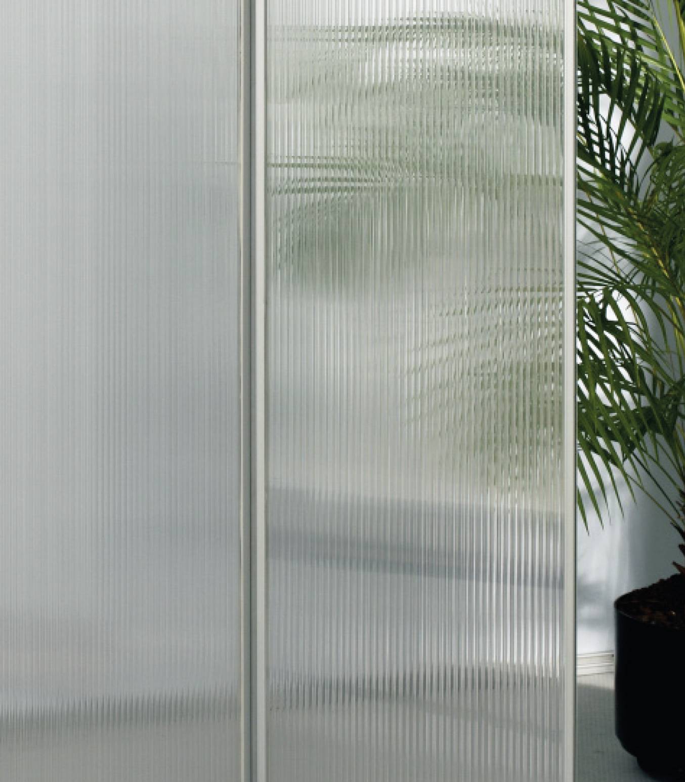Rozmazaná skleněná stěna se stínem rostliny viditelným v pozadí. Scéna působí klidně a minimalisticky.