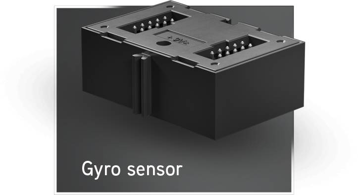 Černý gyroskopický senzor s několika připojovacími piny, označený štítkem "Gyro sensor", na šedém pozadí.