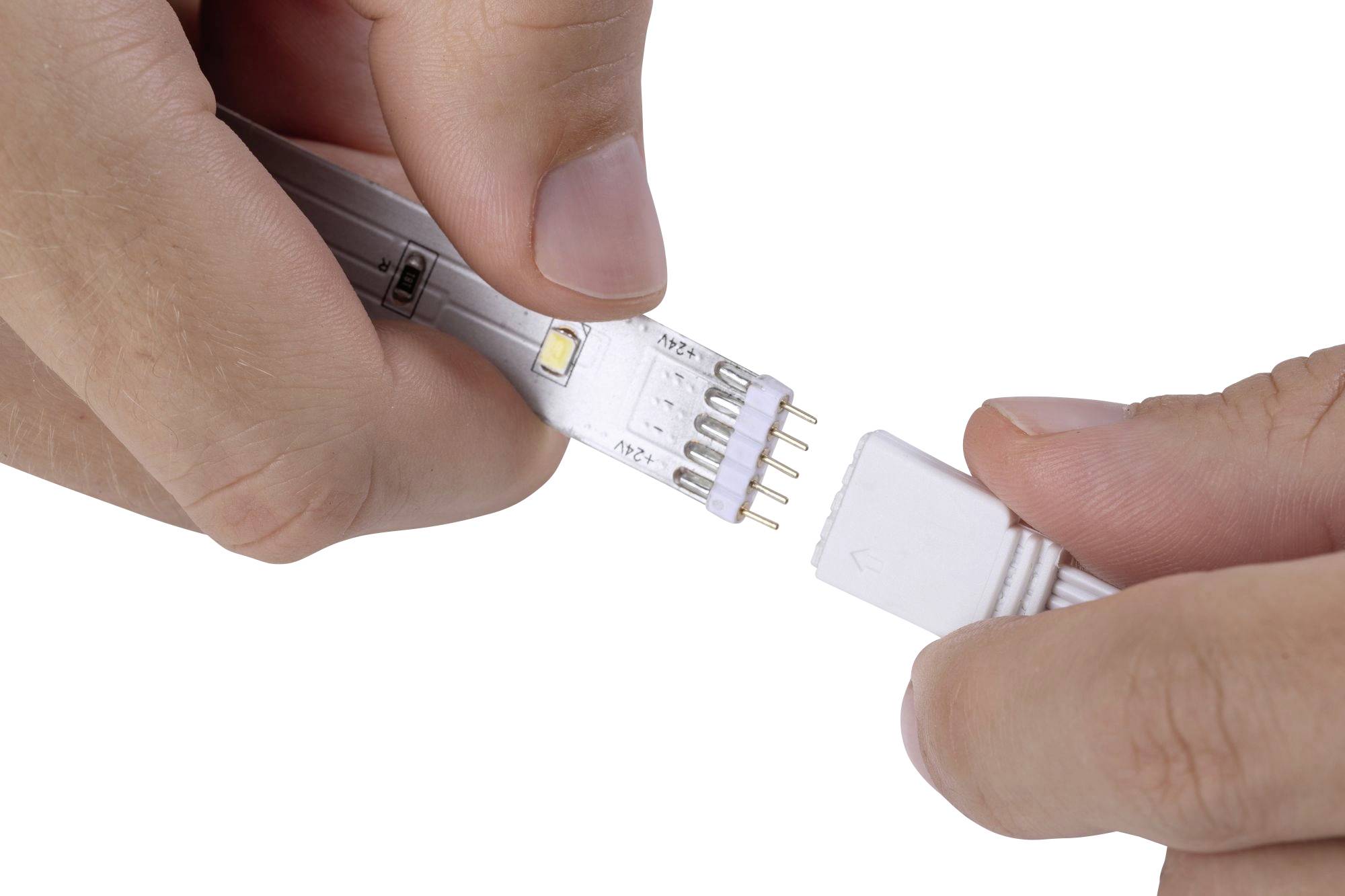 Osoba připojuje LED pásek ke kabelu, aby vytvořila elektrické propojení. Ruce drží oba konce.