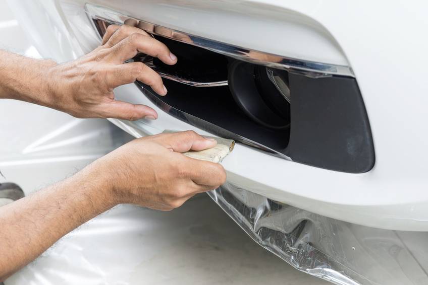 Jedna osoba ručně leští lesklý, bílý nárazník automobilu. Pohyb je opatrný, s malým leštícím hadříkem.