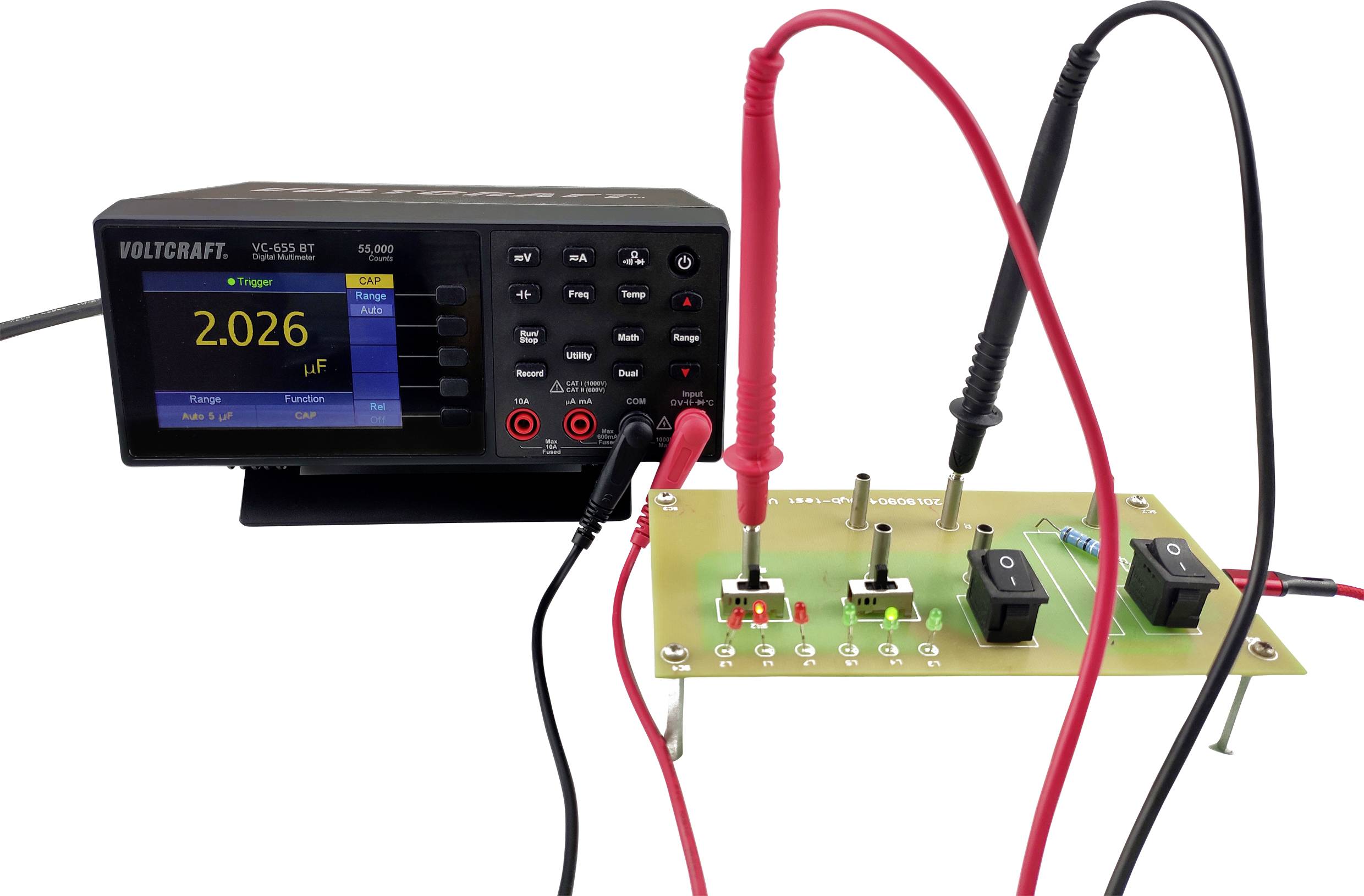 Digitální měřicí přístroj měří elektronické komponenty na desce plošných spojů. Na obrazovce je zobrazeno '2,026 µF'.