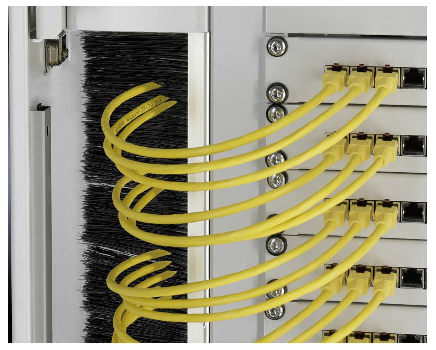 Žluté skleněné optické kabely jsou uspořádány do drážek serverové skříně, vedeny spirálovitě a propojují síťové komponenty.