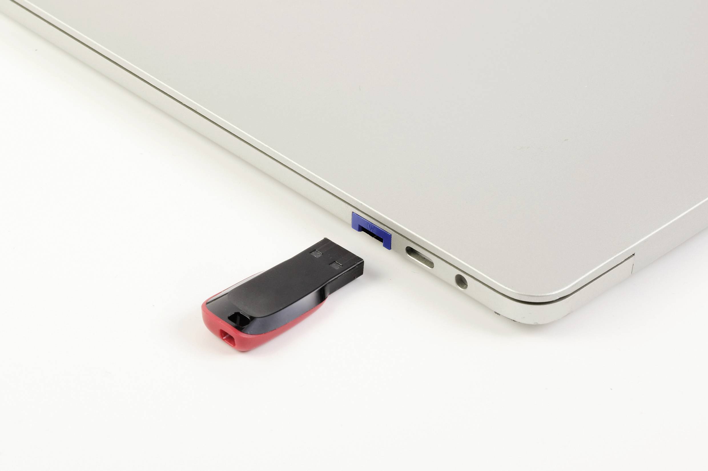 USB flash disk je zasunut do modrého USB portu laptopu. Laptop leží na bílém povrchu.