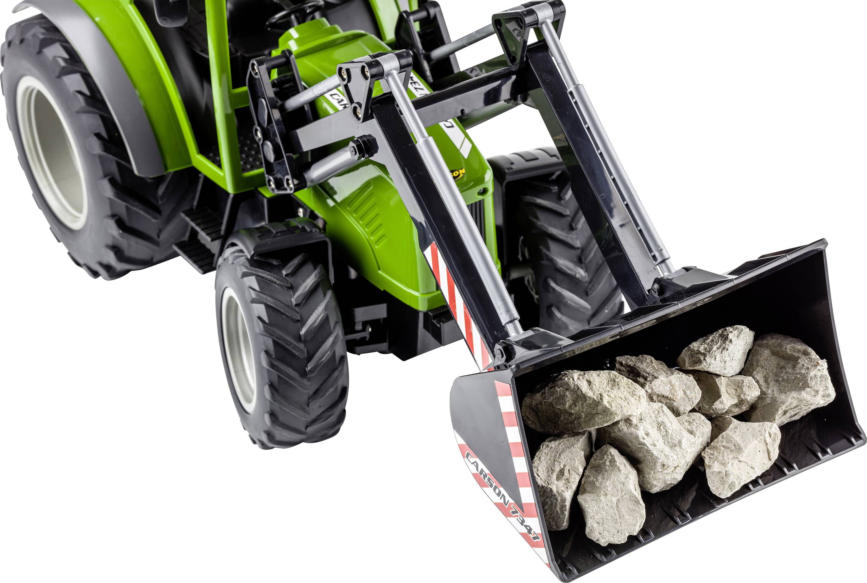 Zelený traktor s čelním nakladačem zvedá lopatu plnou kamenů.