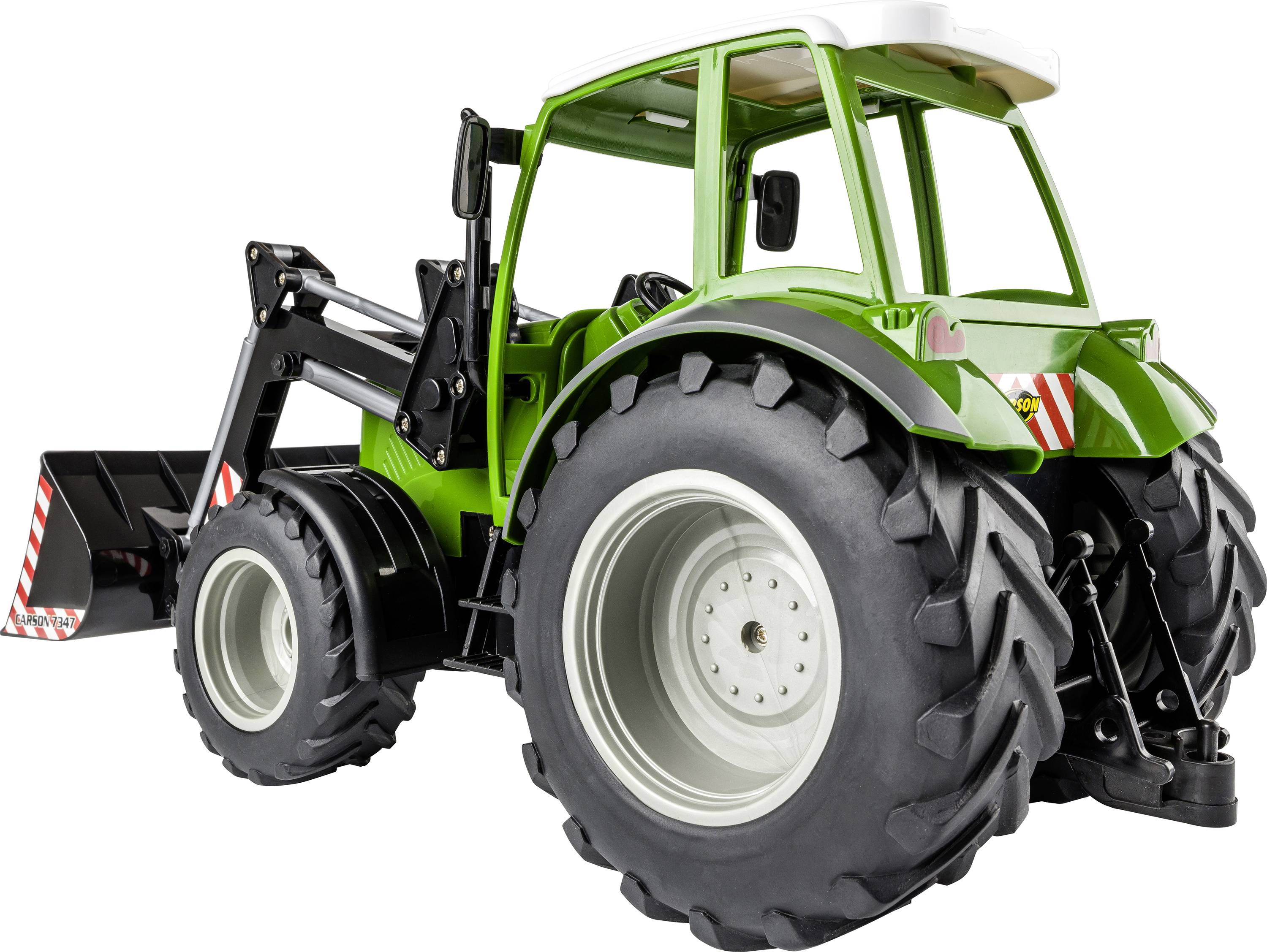 Zelený hračkový traktor s velkými černými koly a čelním nakladačem stojí na bílé ploše.