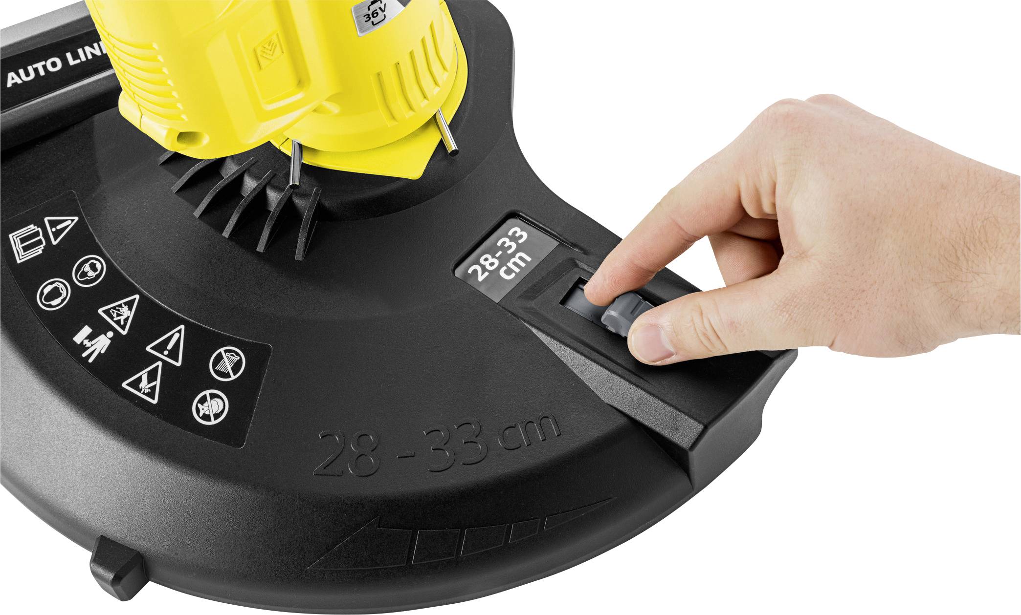 Jedna ruka nastavuje šířku sečení sekačky na '28-33 cm'. Žlutý motor je zčásti viditelný.