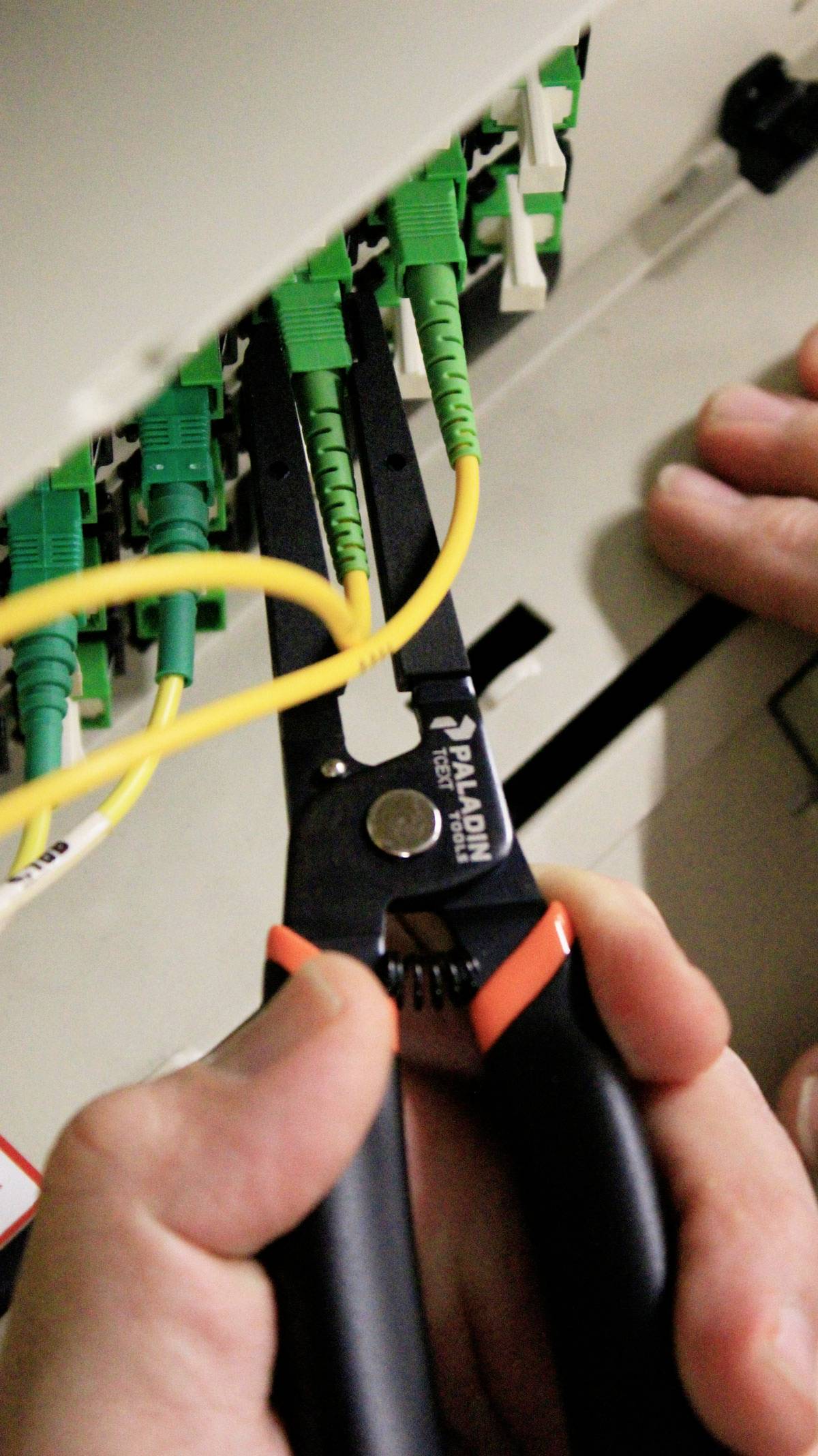 Kleště oddělují žlutý kabel v síťovém rozvaděči; ruce drží nástroj, zatímco zelené kabely zůstávají propojené.