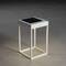 Moderní bílý stůl s čtvercovou skleněnou deskou a minimalistickým designem stojí na hladké šedé podlaze.