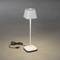 Bílá stolní lampa s USB portem na šedém pozadí. Lampa je zapnutá a kabel leží vedle ní.