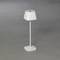 Bílá stolní lampa s moderním, minimalistickým designem na šedém pozadí. Čtvercová základna, štíhlý stojan, trapézovitý stínidlo.