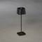 Černá stolní lampa s čtvercovým stínítkem a podstavcem, stojící na šedé podlaze. Moderní, minimalistický design.