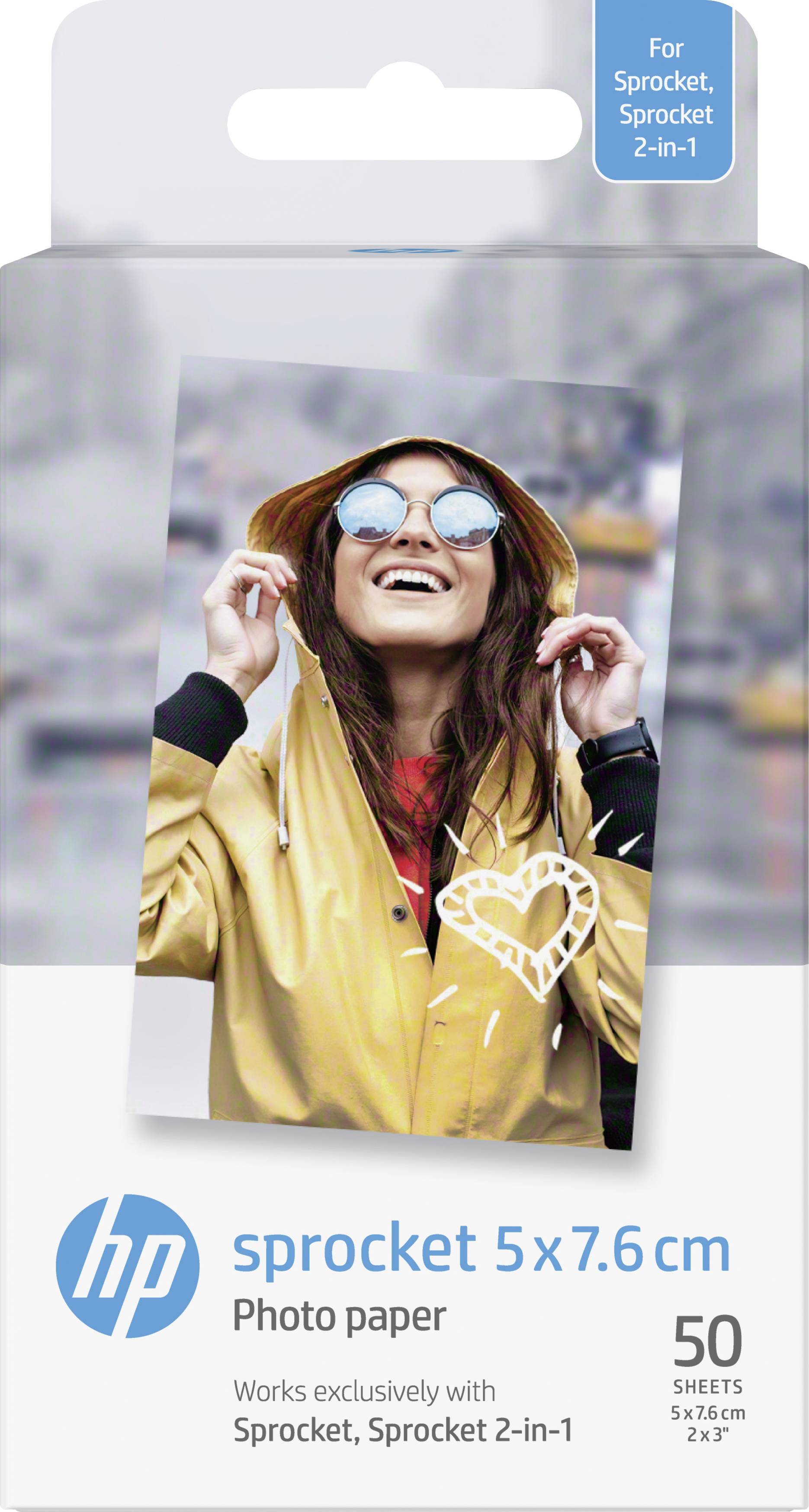 Mladá žena v žluté bundě a slunečních brýlích se usmívá a drží kapuci v městském prostředí. Obal pro fotografický papír HP Sprocket.