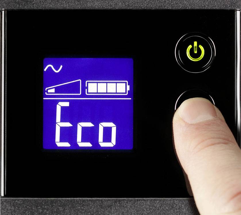 Prst stiskává tlačítko 'Eco' na elektronickém displeji se symbolem baterie a vlnovkou; zelený indikátor zapnutí svítí.