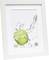 Bílý rámeček vystavuje obraz se zeleným jablkem, které je zasaženo postříkáním vody. Rozměr: 20x30 cm.