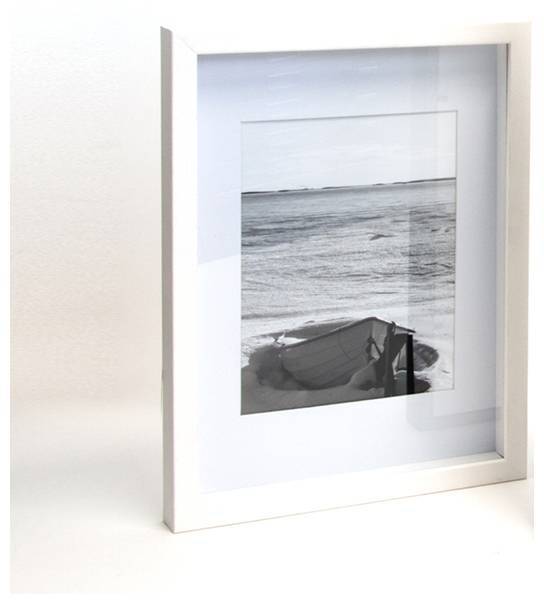 Zarámovaná černobílá fotografie lodi na pláži s vlnami v pozadí. Obraz je položen šikmo na bílém podkladu.