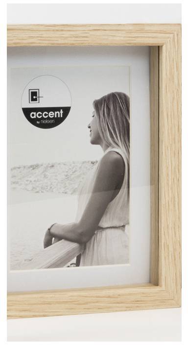 Osoba stojí venku u zábradlí a dívá se do dálky. Obraz je v dřevěném rámu a má logo 'accent' od 'nielsenu'.