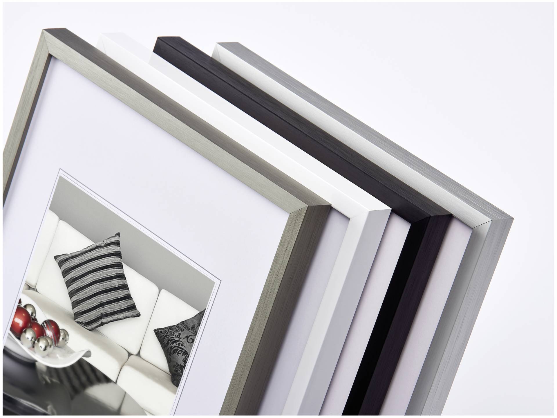 Rámy v různých barvách a velikostech, navršené přes sebe. Přední rám zobrazuje fotografii gauče s polštáři.