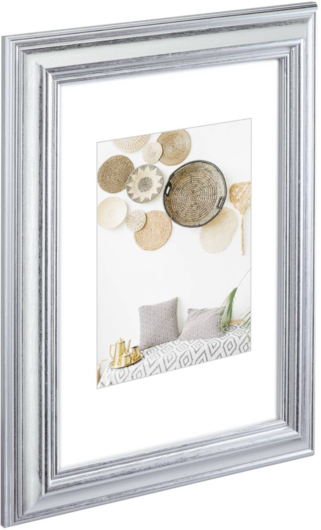 Stříbrný rámeček vystavuje fotografii košů na stěně nad postelí s šedými polštáři a geometrickou přehozkou.