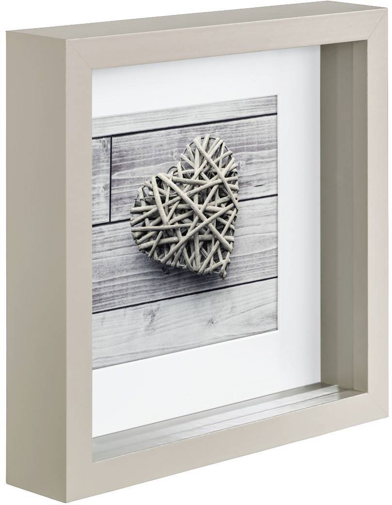 Zarámovaný obraz dřevěného srdce na dřevěné stěně; srdce je složené z propojených větví, rám je jednoduchý a béžový.