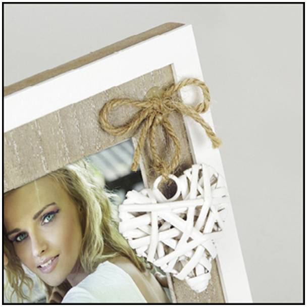 Dřevěný fotorámeček s dekorativní mašlí a srdíčkovým přívěskem z bílého materiálu. Součástí snímku je část fotografie osoby.