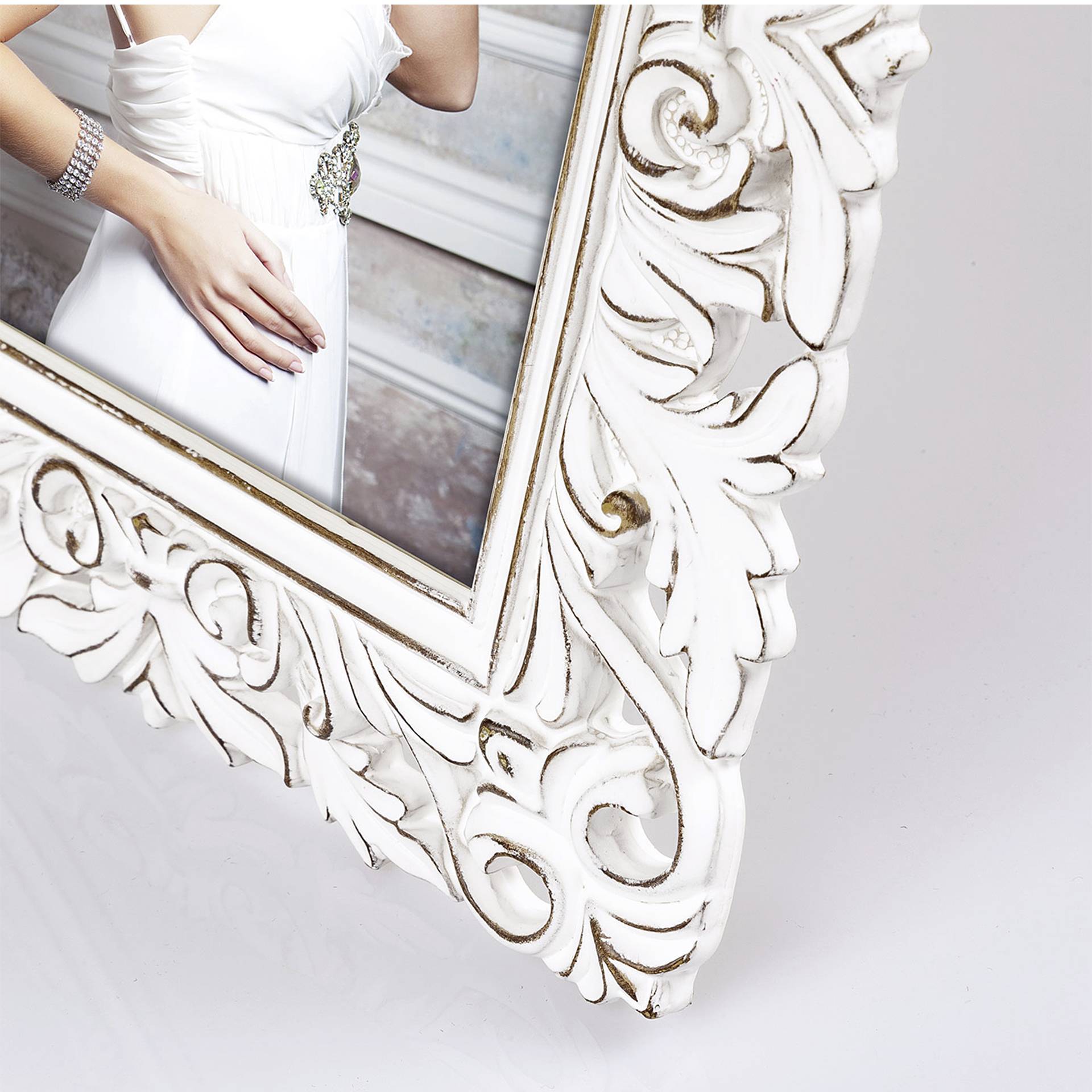 Žena v bílých šatech se stříbrnou ozdobou pózuje v umělecky zdobeném bílém rámu obrazu.